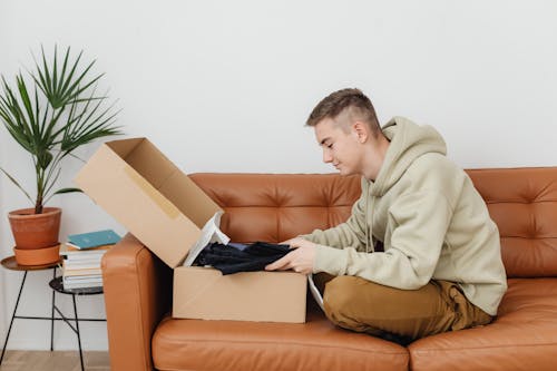 Free Man Sitting on Couch Unboxing Clothes  Stock Photo