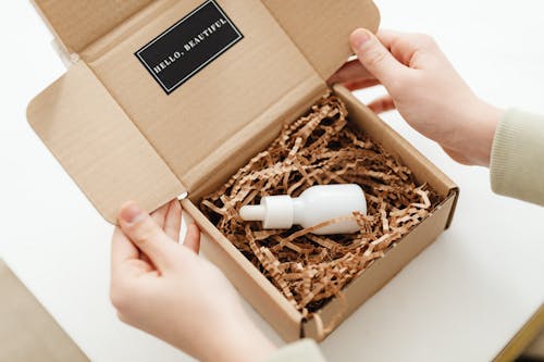 Free Hands of a Person Opening a Box with a White Bottle Stock Photo