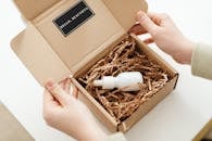 Hands of a Person Opening a Box with a White Bottle