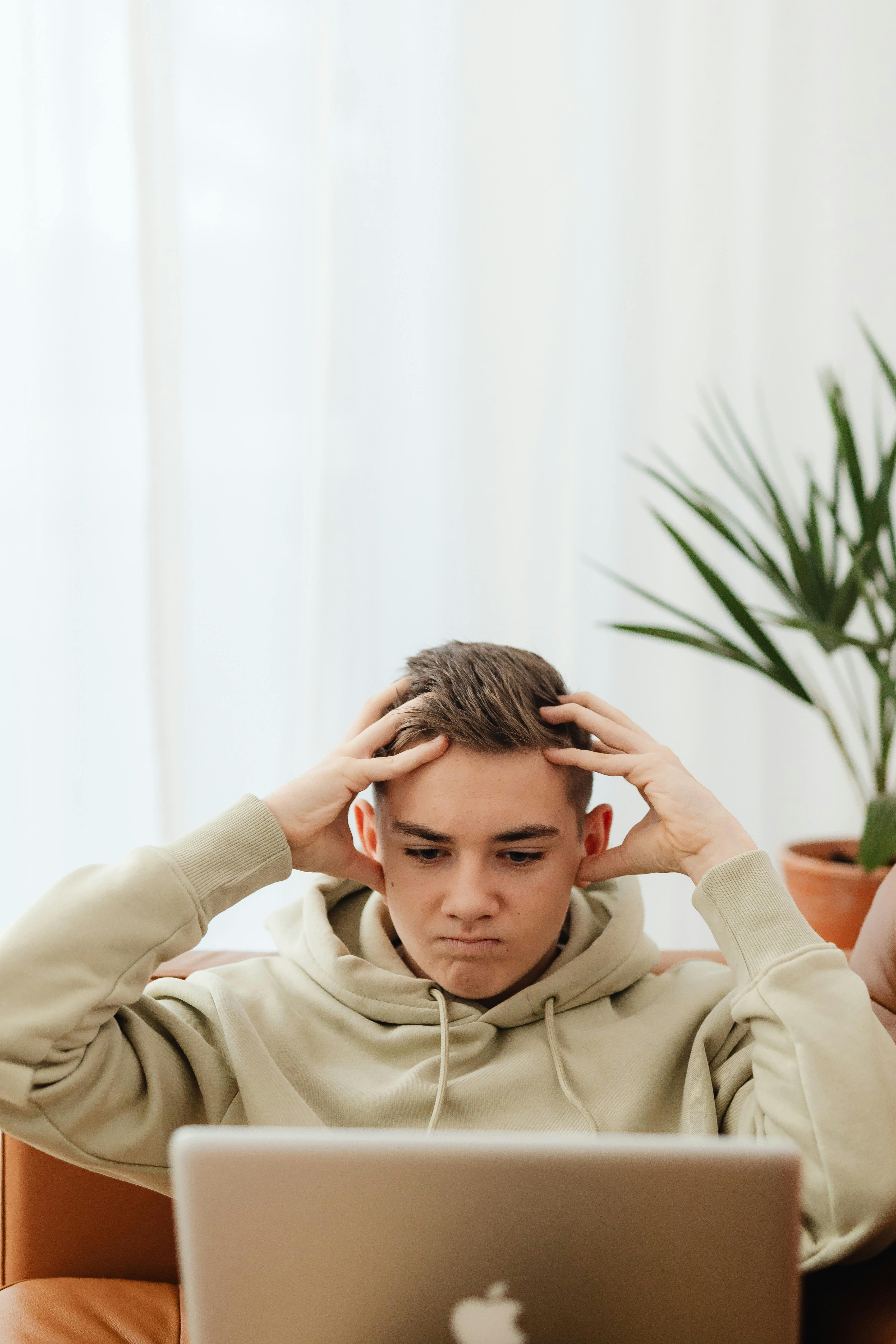 man wearing hoodie with hands on head while using laptop