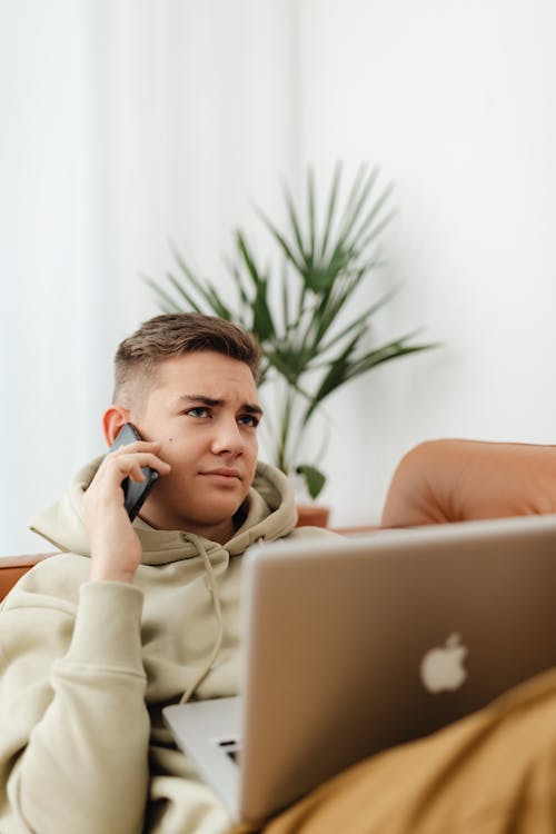 Free Man Using a Smartphone and Laptop While Sitting on a Couch Stock Photo