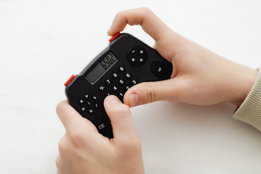 Close-up of hands using a portable black calculator with a digital display on a white background.
