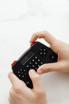 Close-up of hands holding a small, black electronic calculator with a digital display.