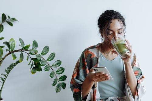 A Woman Drinking Matcha while Using Her Mobile Phone