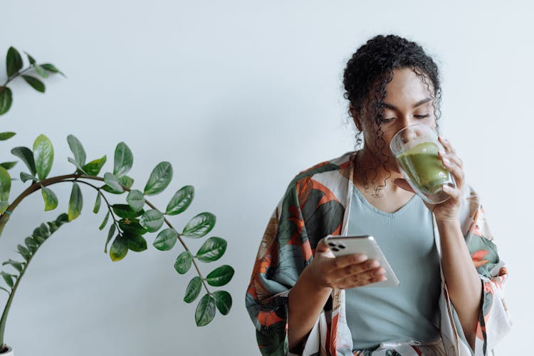 A Woman Drinking Matcha While Using Her Mobile Phone