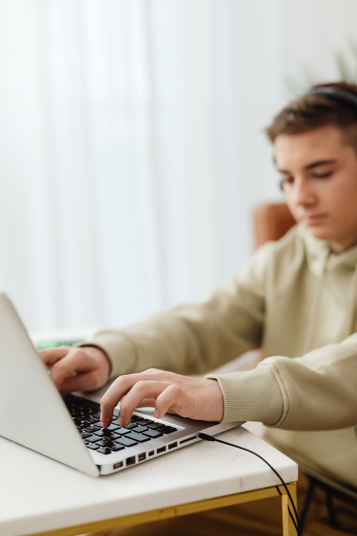 Teenage boy wearing headphones, focused while typing on a laptop