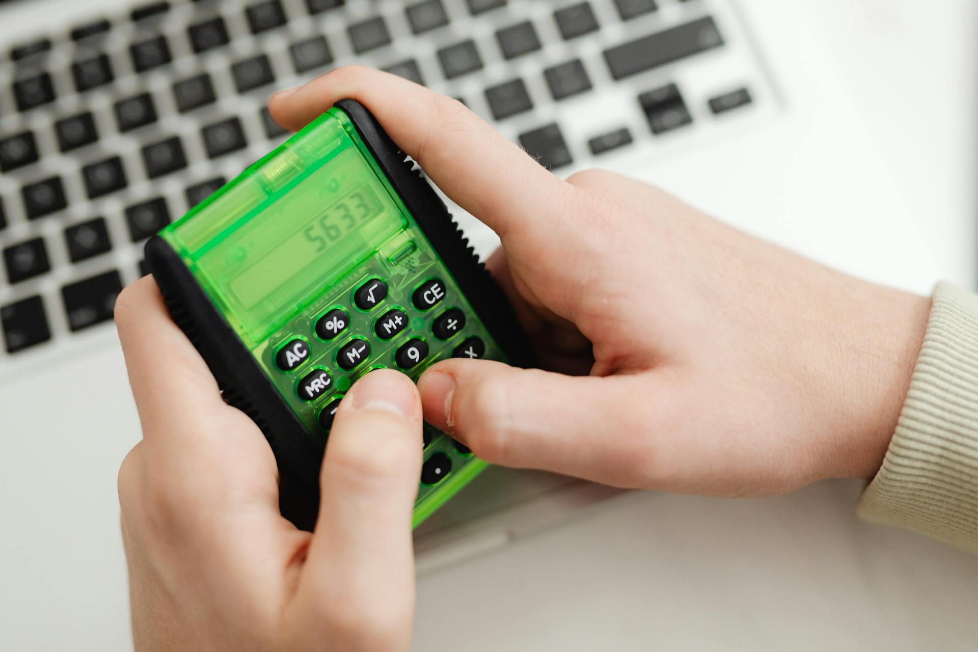 Close-up of hands using a green calculator near a laptop. Modern finance concept.