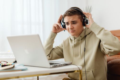 Free A teenage boy wearing headphones is engaged with a laptop in a cozy home environment. Stock Photo