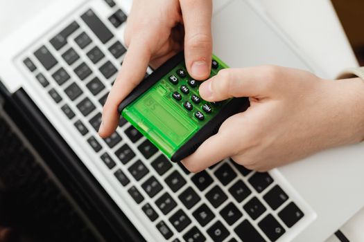 Hands using a green calculator on a laptop keyboard, representing business and finance tasks.
