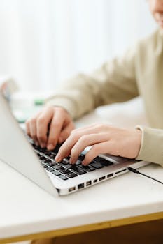 Close-up of hands typing on a laptop, showcasing remote work indoors.