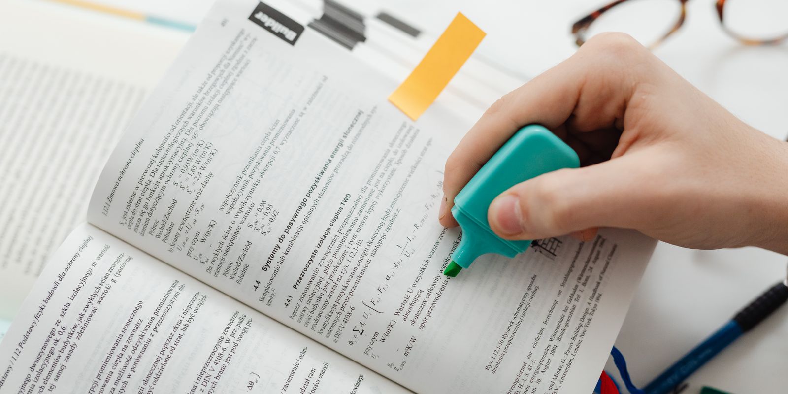 A hand highlighting text in a printed document with a teal highlighter