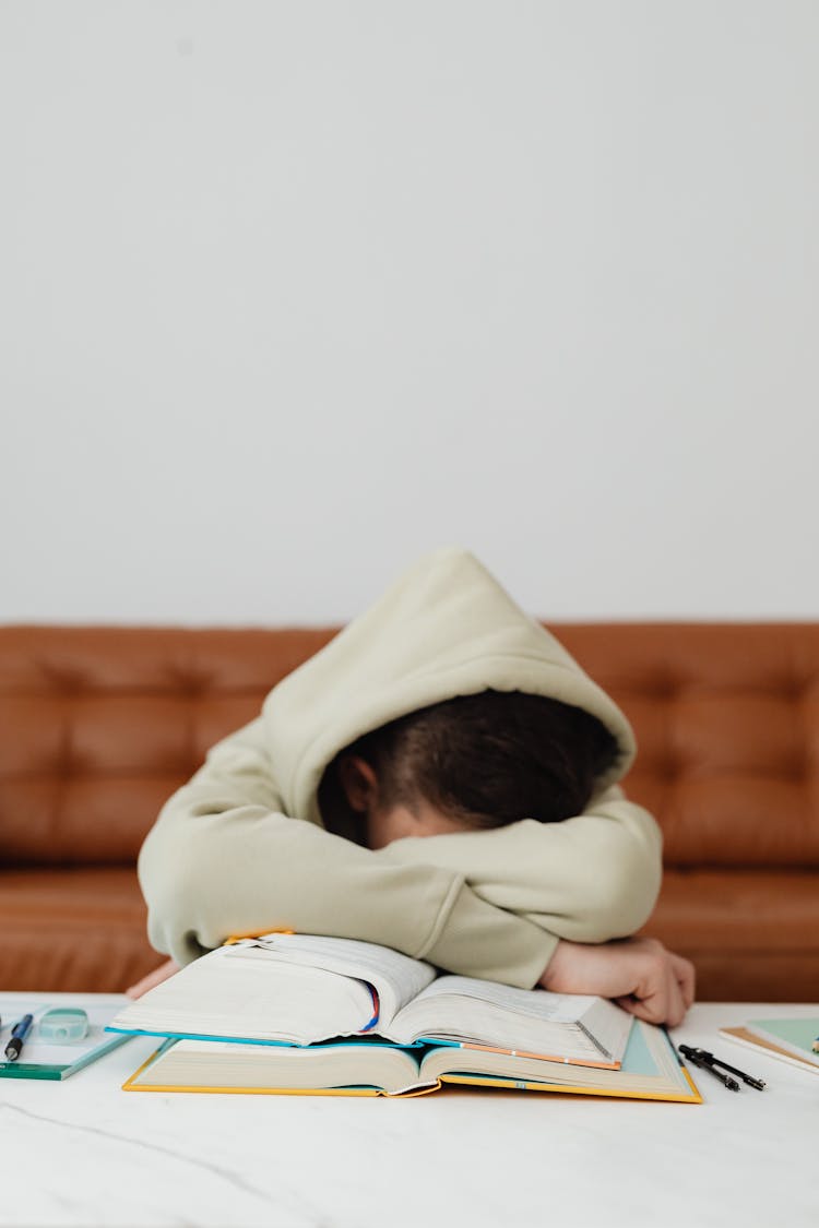 Child In Beige Hoodie Leaning Forward On Table Feeling Tired