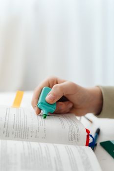 A hand highlighting text in a book using a green marker.