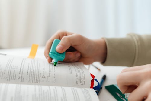 Person Using Blue Highlighter Pen On A Book Page