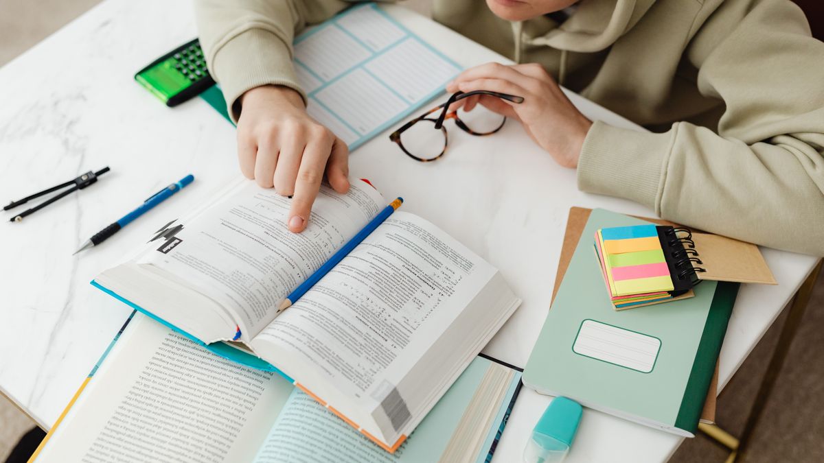 Estudante concentrado estudando com livros, calculadora e anotações sobre a mesa