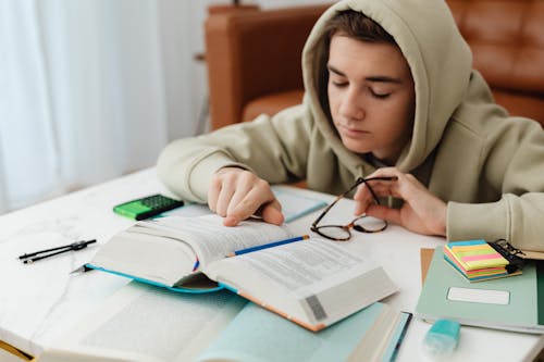 Young Man In Beige Hoodie Reading And Studying At Home