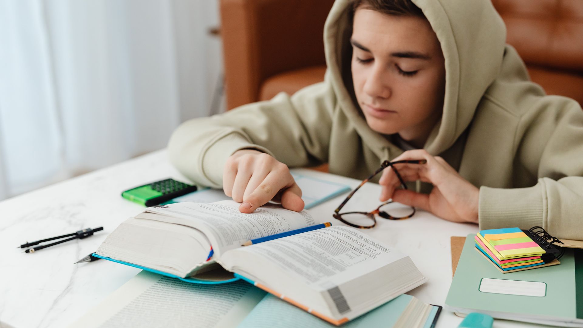 Modafinil for Studying: Boost Your Academic Performance A teenager in a hoodie studying with books and notes on a table, focused on learning indoors.