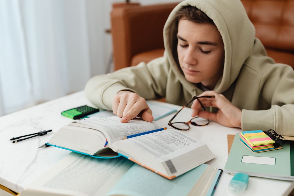 Jovem estudando em casa com livros e caderno, aprendendo educação financeira
