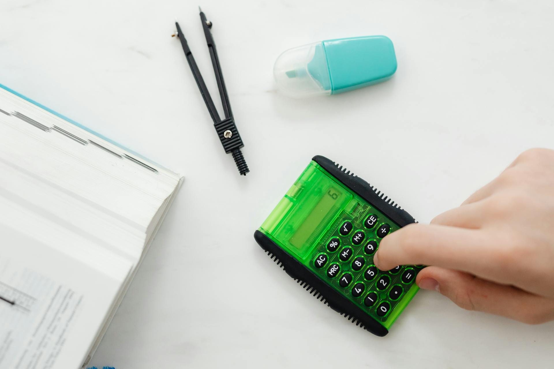 Close-up of a hand using a green calculator with stationery for studies or business calculations.