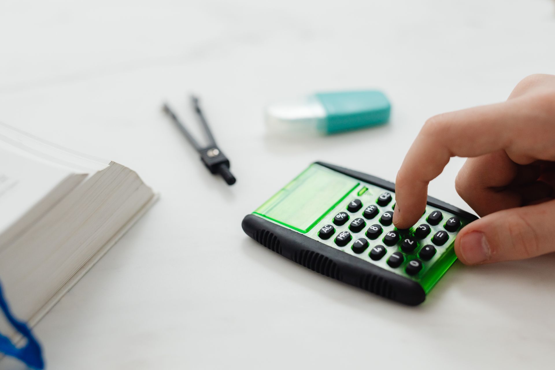 Close-up of a person's hand pressing a calculator on a desk with other stationery items.