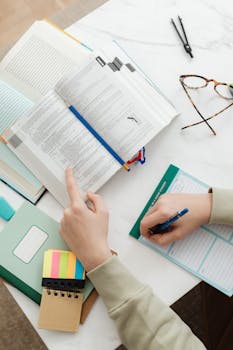 Close-up of a student studying with books and notes on a white desk.