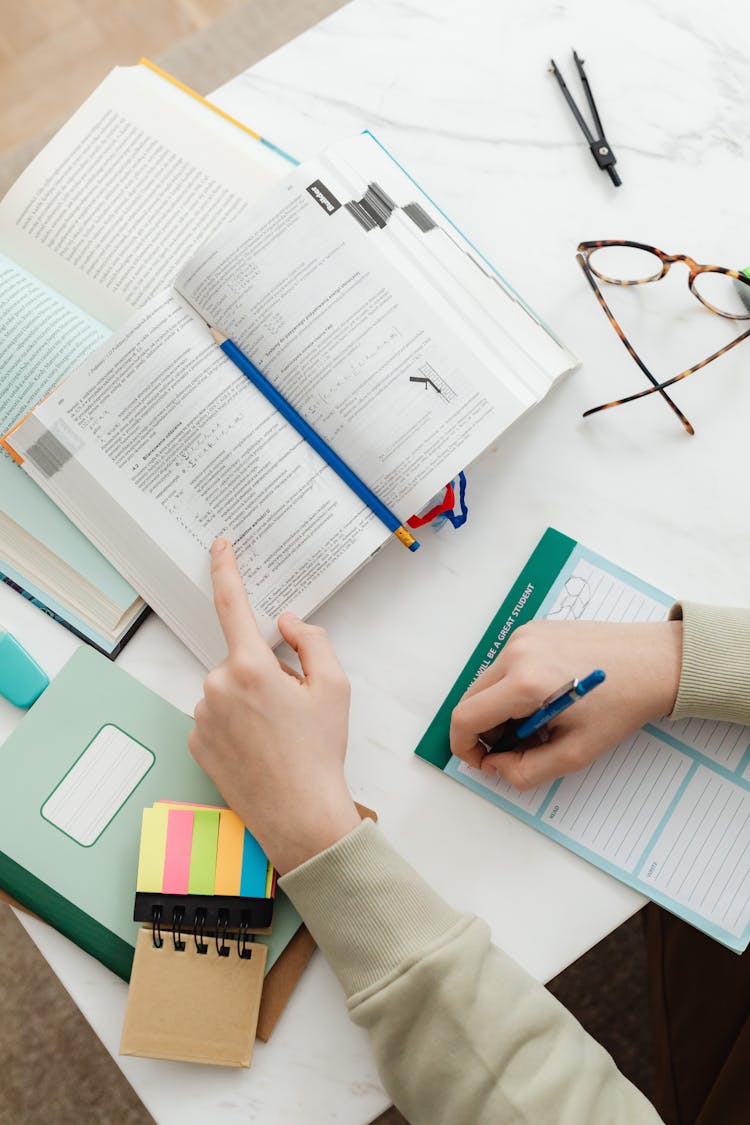 Close-up Of Person Sitting At Desk Studying With Textbooks