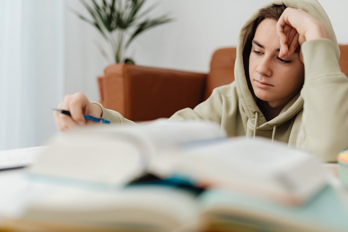 Free Student Wearing Hood and Books in Foreground Stock Photo