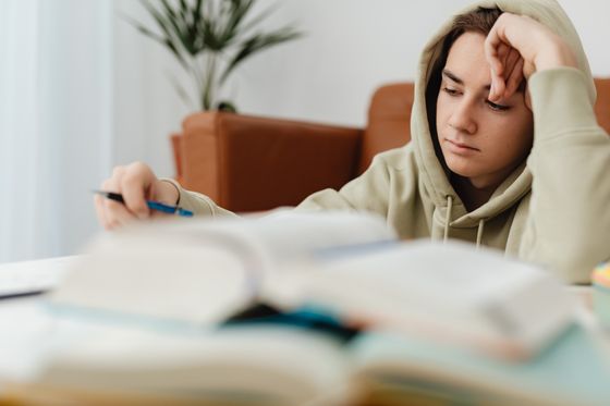 A teenager in a hoodie reading and writing at home — photo by Kaboompics on Pexels