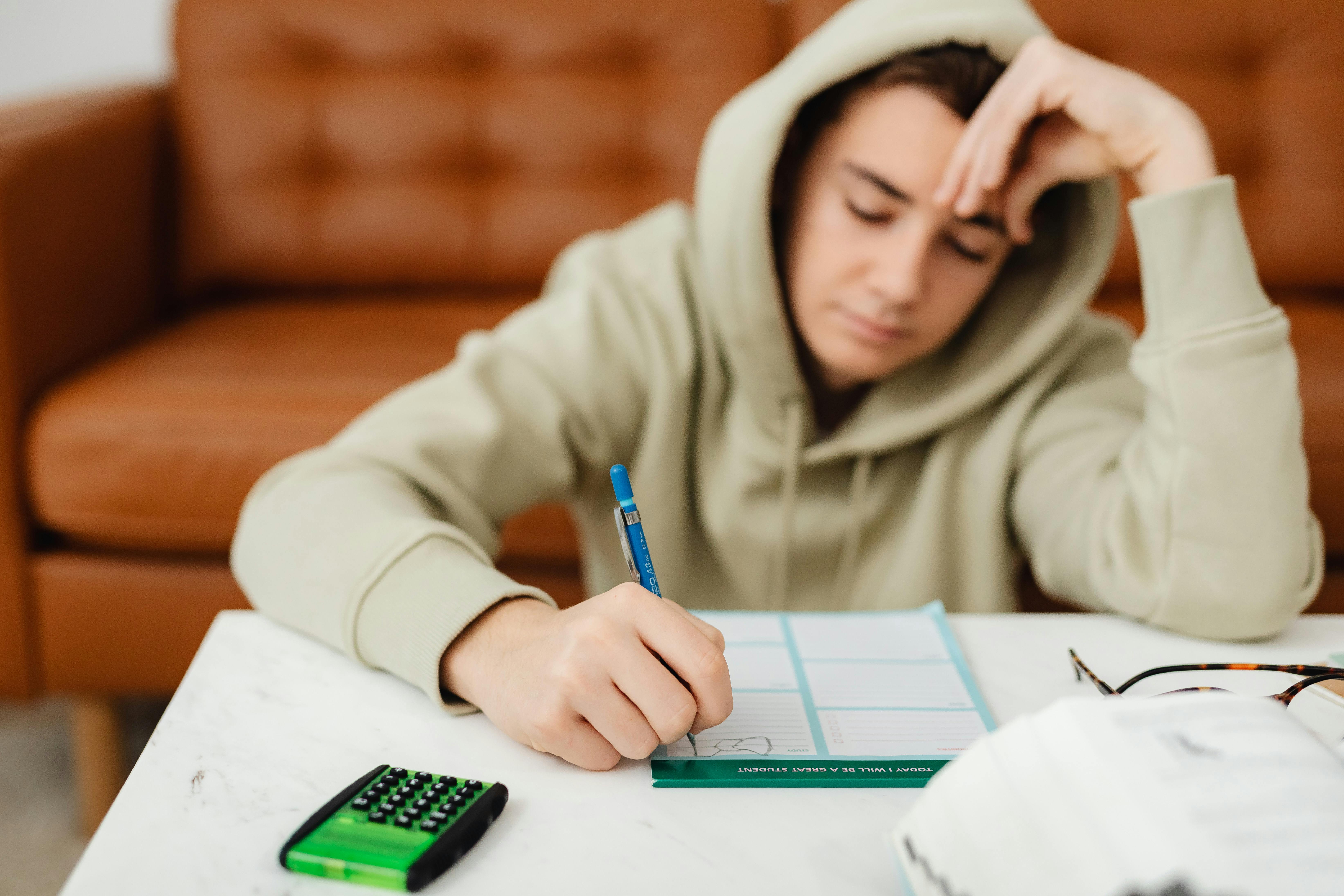 selective focus photo of a boy in a hoodie writing on a paper