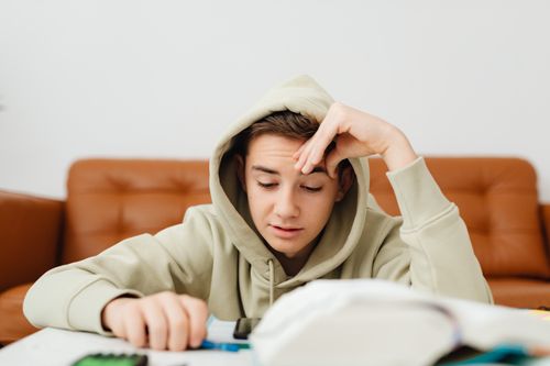 Free Focus on a teenage boy studying indoors, wearing a hoodie, symbolizing concentration and learning. Stock Photo