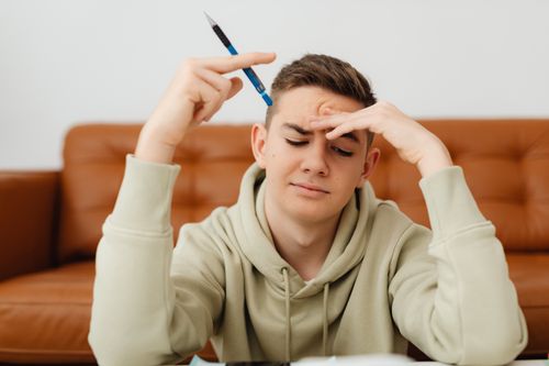 Free A stressed teenager in a hoodie struggles with homework, deep in thought indoors. Stock Photo