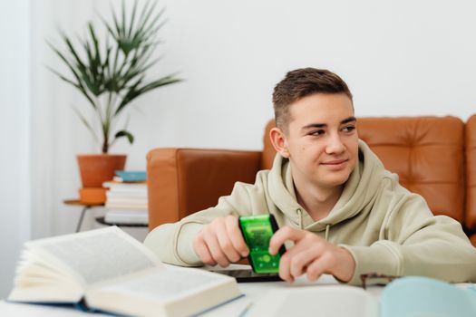 Young man in a hoodie studying at home using a calculator and open book.