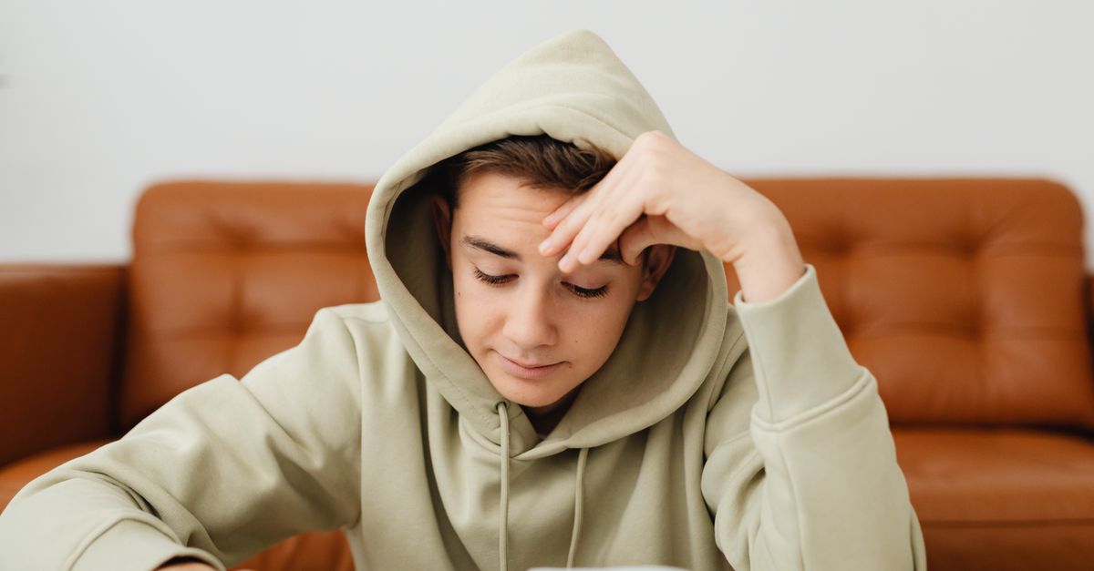 A teenager deeply focused on a notebook or book, no phone in sight, in a quiet room
