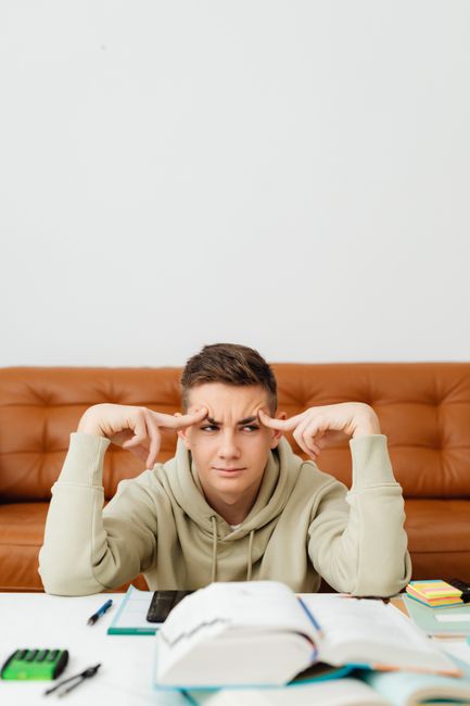 A teenager sits at home studying with a confused expression, surrounded by textbooks. A teenager sits at home studying with a confused expression, surrounded by textbooks.