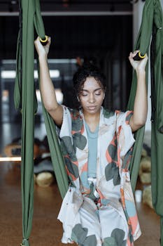Young woman practicing aerial yoga with green hammocks in indoor studio setting.