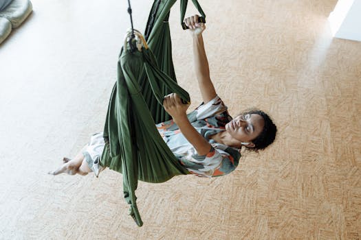 Woman practicing aerial yoga in a green hammock indoors, fostering relaxation and fitness.