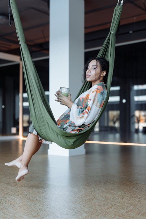 Woman in White and Green Floral Dress Sitting on Green Hammock
