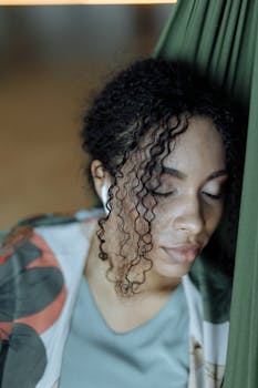 Peaceful woman with air pods resting in a hammock, capturing tranquility indoors.