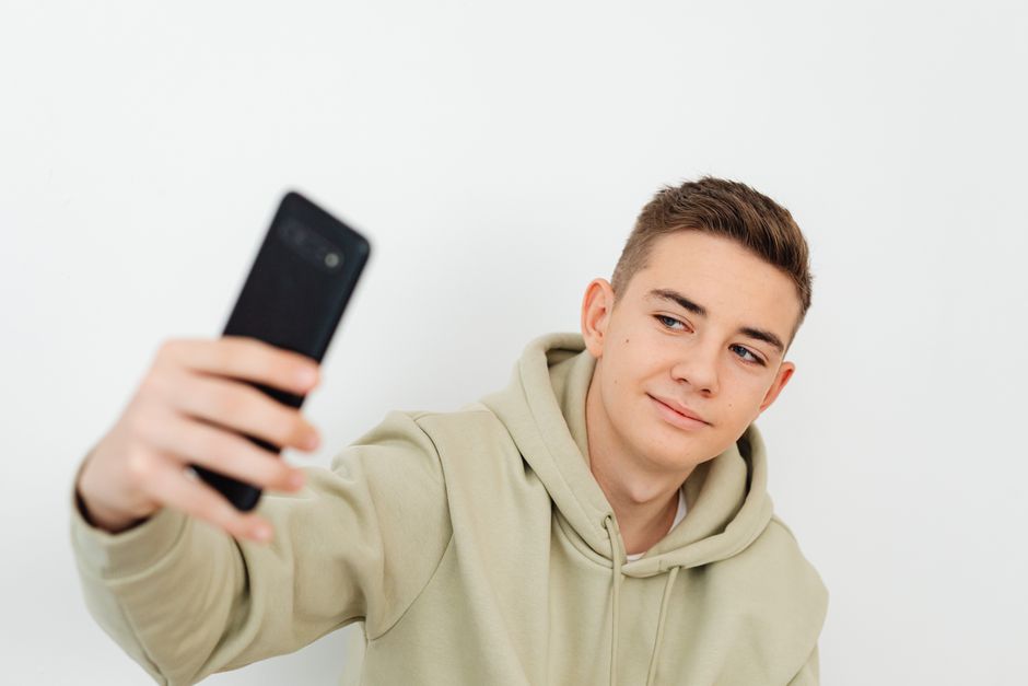 Teenager in hoodie taking a selfie indoors with a smartphone.