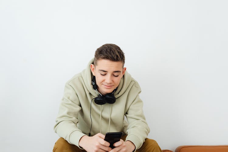 Man With Headphones Around His Neck Using Cell Phone