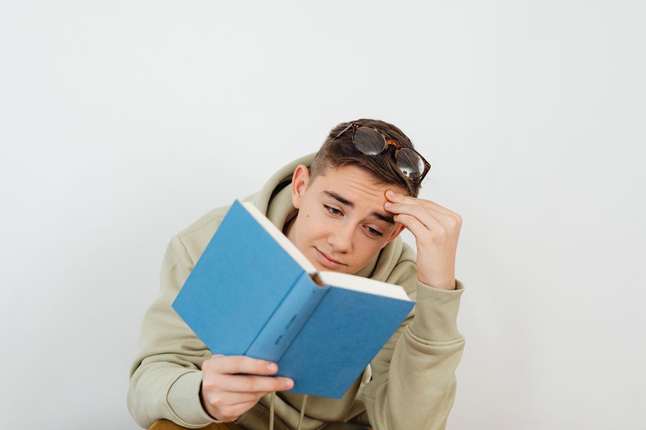 Teenager reads a book while holding glasses on his head, against a plain white background. Teenager reads a book while holding glasses on his head, against a plain white background.