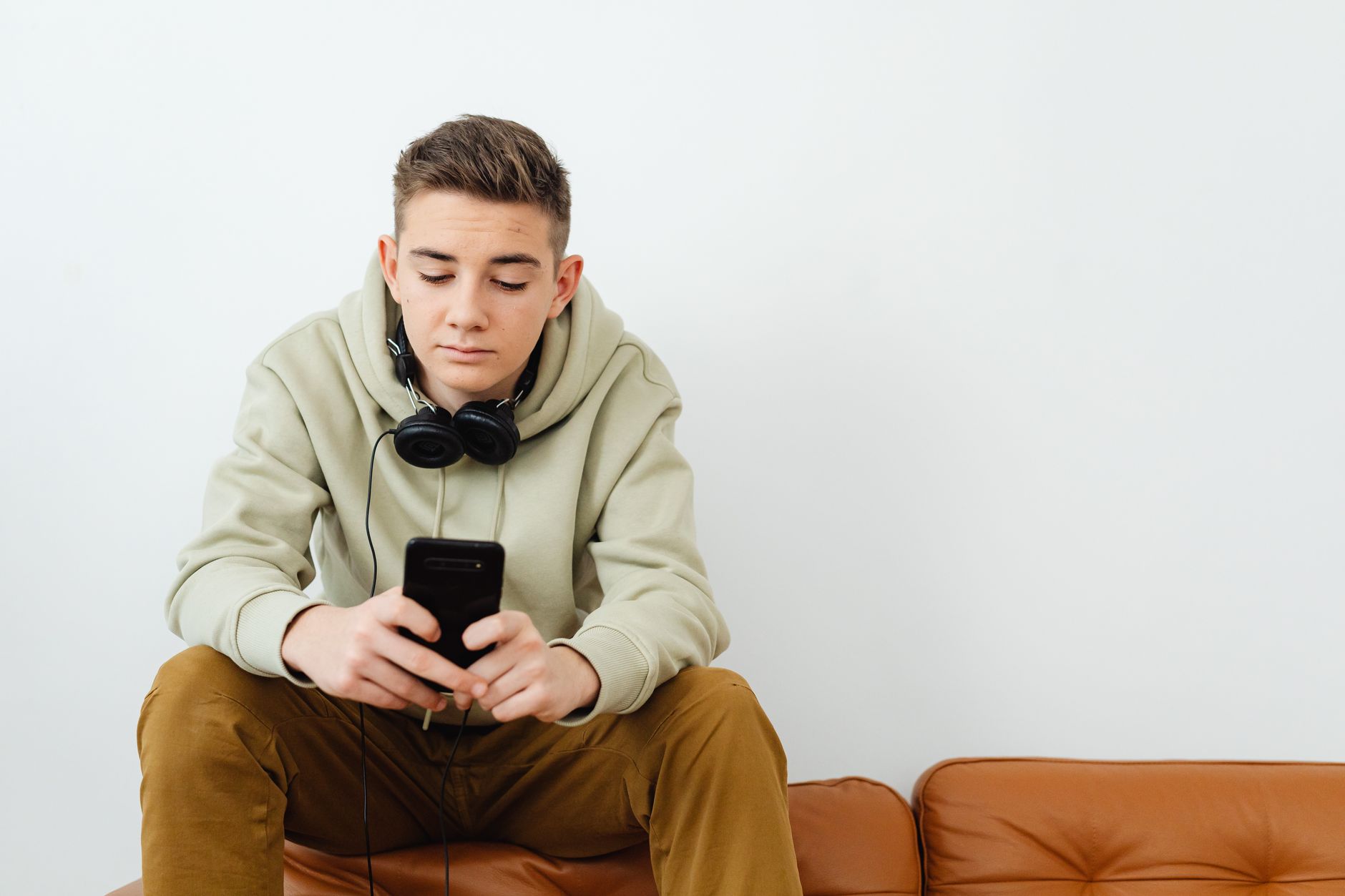 A teenage boy sits on a couch looking at his smartphone, illustrating youth online activity relevant to concerns about technology-facilitated abuse.