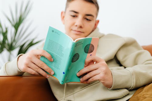 Teenage Boy Reading a Book and Sitting on a Couch 