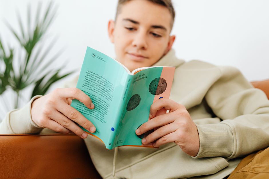 A relaxed teenage boy reading a book on a comfortable sofa, enjoying leisure time.