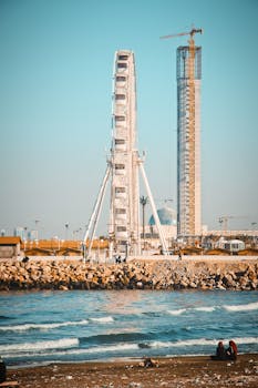 在阿尔及利亚的海岸线上，摩天轮和建筑塔矗立着，海浪拍打着海滩