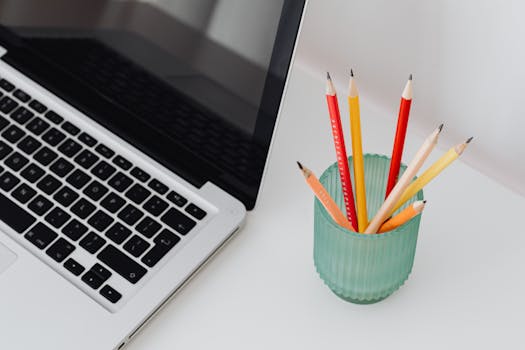 High-angle view of a laptop and vibrant pencils in a glass cup, a perfect modern workspace setup.