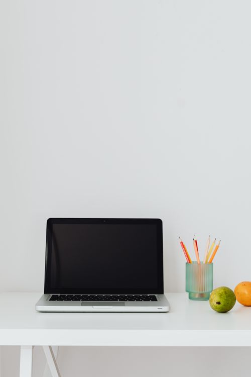 Free A clean and minimalist workspace featuring a laptop, citrus fruits, and pencils on a white table. Stock Photo