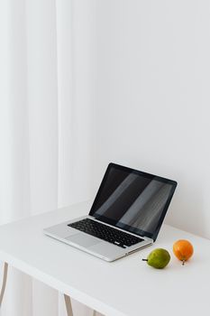 A sleek laptop on a white desk with fruits, showcasing a minimalist workspace design.