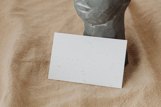 A minimalist blank card mockup positioned against a cloth and stone bust for design presentations.