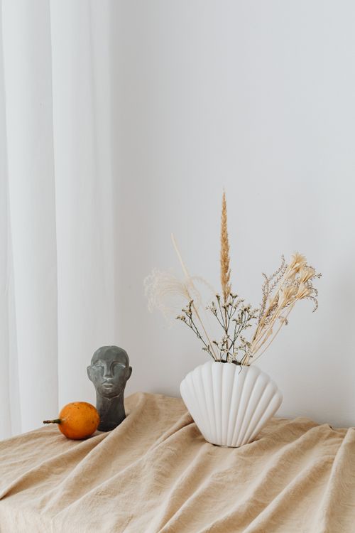 Free A still life composition featuring dried flowers in a shell-shaped vase and artistic elements on a neutral fabric surface. Stock Photo